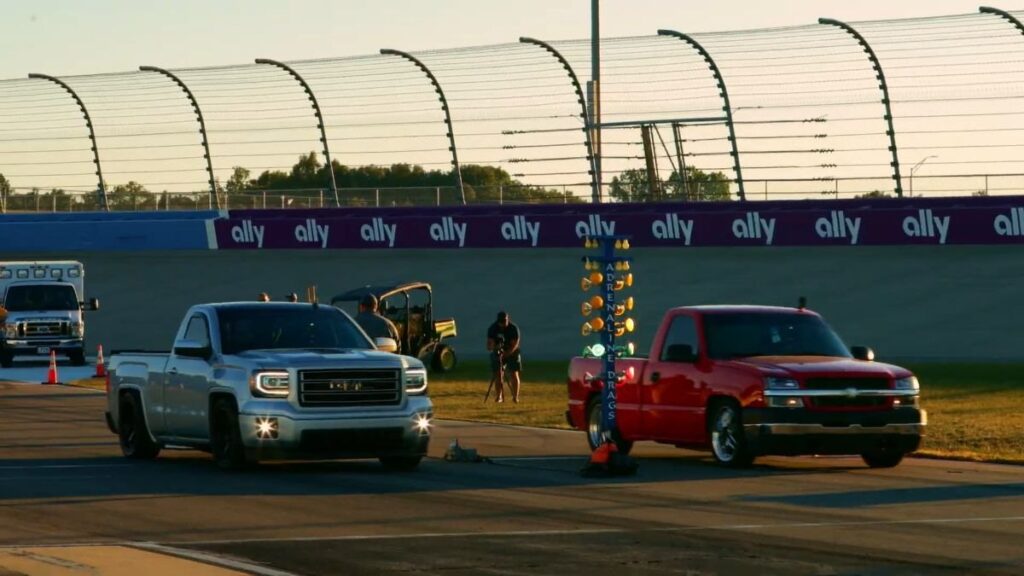 Drone video still of trucks on a racetrack in front of grandstands